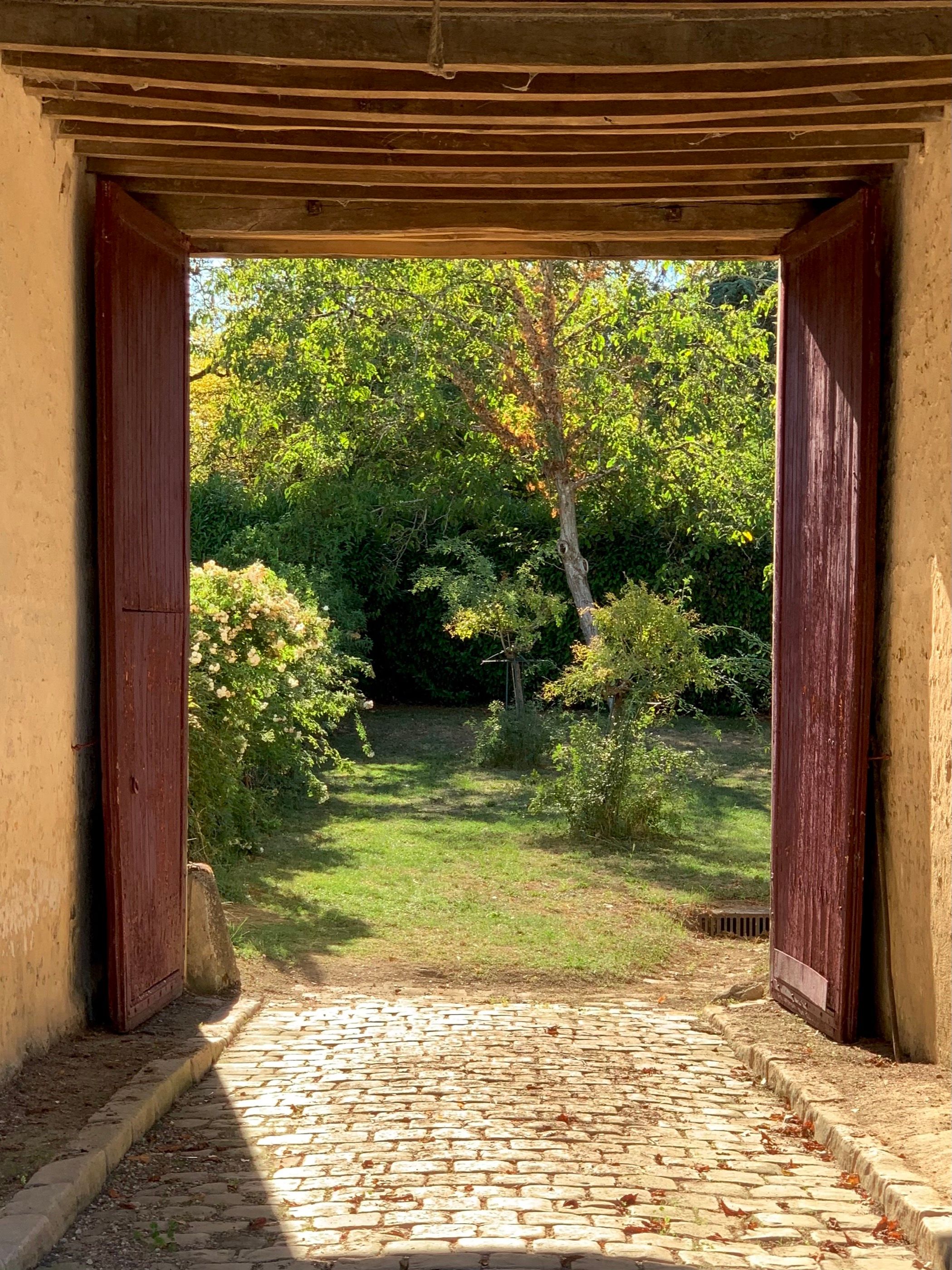 Le porche du domaine ouvert sur le jardin, lumière du soir et pavés anciens